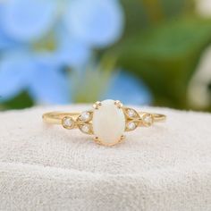 a white opal and diamond ring sitting on top of a cloth covered cushion with blue flowers in the background