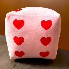 a pink bag with red hearts on it sitting on a wooden table in front of a brown wall