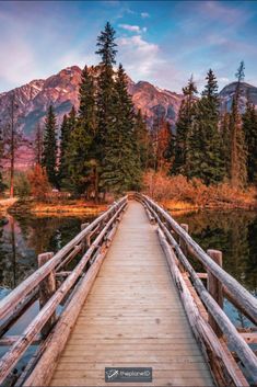 a wooden bridge over a body of water with mountains in the background and trees on both sides