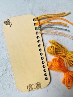 a wooden bookmark with two strings attached to it and an orange string next to it