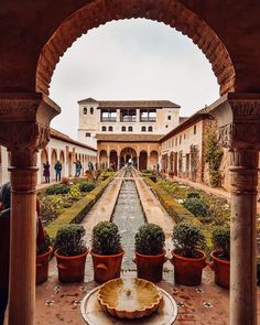 an outdoor courtyard with potted plants and water fountain in the center, surrounded by stone arches