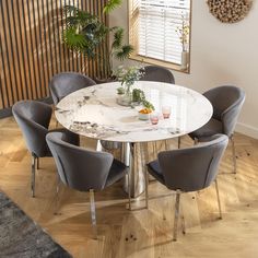 a white marble dining table surrounded by grey chairs in a room with wood flooring