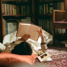 a person laying on the floor reading a book in front of a bookshelf