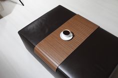 a coffee cup is sitting on top of a black and brown leather ottoman that sits on a white floor