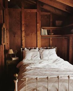 a bed with white linens and pillows in a rustic style bedroom setting, along with bookshelves