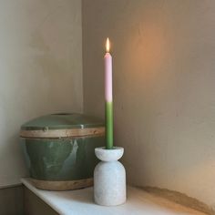 a candle sitting on top of a white shelf next to a green bowl and container