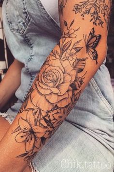 a woman's arm with flowers and butterflies tattooed on the arm, while sitting down