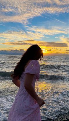 a woman in a pink dress is standing on the beach looking out at the ocean