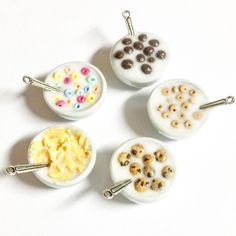 four miniature bowls filled with cereal and other items on a white surface, all decorated in different colors