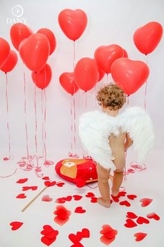 a small child dressed as an angel surrounded by red balloons