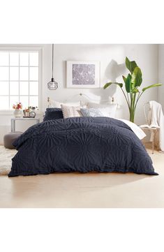 a bedroom with white walls and blue comforter on the bed, along with potted plant