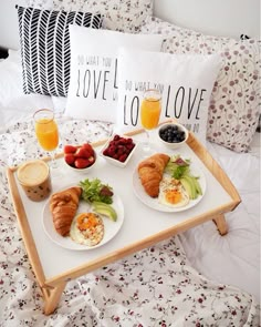 two trays filled with breakfast food on top of a bed next to pillows and pillow cases