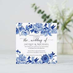 a blue and white floral wedding card on a table next to a vase with flowers