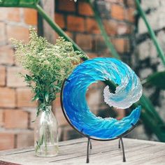 there is a vase with flowers in it next to a blue glass wave on a stand