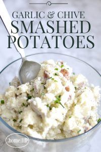 garlic and chive smashed potatoes in a glass bowl with a spoon on the side