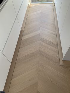 an empty kitchen with wood flooring and white cupboards on the side walk way