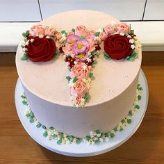 a white cake with pink and red flowers on the top is sitting on a wooden table