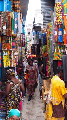 people walking through an open market with colorful fabrics