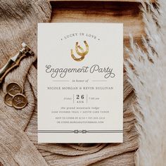 an engagement party card on top of a fur rug next to two gold rings and a pair of scissors