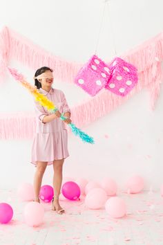 a woman standing in front of pink balloons and streamers with two dices hanging from them