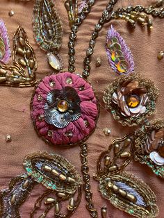 an assortment of brooches and beads on a pink cloth with gold trimming