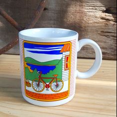 a white coffee mug with a bicycle on the front and side, sitting on a wooden table