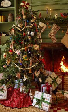 a christmas tree with presents under it in front of a fire place and stockings on the mantle