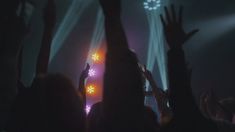 a crowd of people at a concert with their hands in the air and lights on