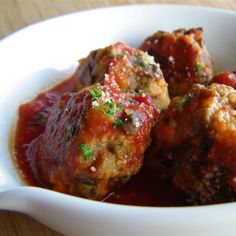 three meatballs in marinara sauce in a white bowl on a wooden table top