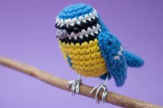 a small crocheted bird sitting on top of a wooden branch with purple background