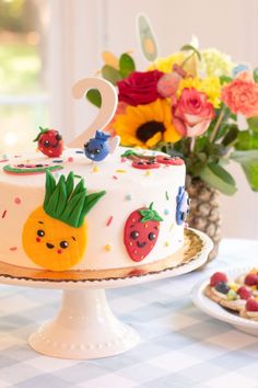 a birthday cake decorated with fruit and flowers on a table next to a vase full of flowers