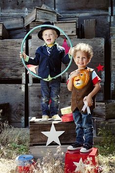 two young boys standing on top of wooden crates holding hoop and pumpkins in front of them