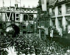 an old black and white photo of people in the street with flags flying from buildings