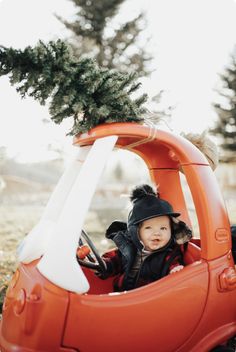 a small child sitting in an orange car with a christmas tree on the back seat