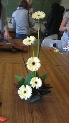 some white flowers are in a vase on a wooden table with other people sitting around