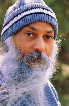 an old man with a long beard wearing a blue hat and sweater is looking at the camera