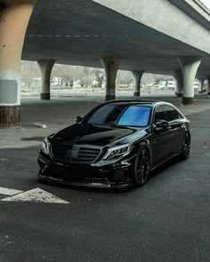 a black mercedes s - class is parked in an empty parking lot under a bridge