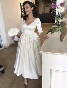 a woman in a white dress standing next to a counter with flowers on top of it