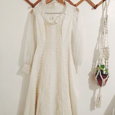 a white dress hanging on a wall next to a potted plant and necklaces