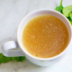 a cup of liquid sitting on top of a table next to some green leafy leaves