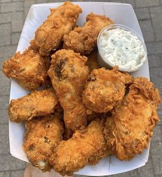 a person is holding a plate of fried chicken with ranch dressing on the side and dipping sauce