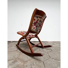 a wooden rocking chair with floral fabric on the seat and backrest, sitting on a tile floor