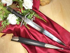 two swords are sitting on a red cloth with white flowers and greenery in the background