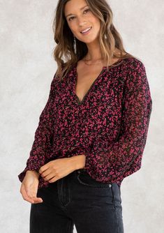 [Color: Black/Raspberry] A model wearing a holiday inspired black and red ditsy floral print chiffon peasant top. With gold thread trim throughout V-neck Ditsy Floral Print Blouse For Fall, Ditsy Floral Print V-neck Blouse For Fall, Fall V-neck Blouse With Ditsy Floral Print, Fall Ditsy Floral Print V-neck Blouse, Feminine Long Sleeve Blouse With Ditsy Floral Print, Bohemian Long Sleeve Blouse With Ditsy Floral Print, V-neck Ditsy Floral Print Top For Brunch, Bohemian V-neck Top With Ditsy Floral Print, V-neck Tops With Ditsy Floral Print For Brunch