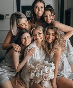 a group of bridesmaids hugging each other and posing for a photo in their wedding gowns