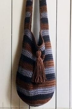 a crocheted bag hanging on a wall with a hook in the middle that has a tasseled handle