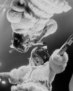 two women in fur coats on stage with one holding a microphone and the other pointing at something