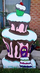 a cardboard cake that is sitting on the ground in front of a brick building with a cupcake on top