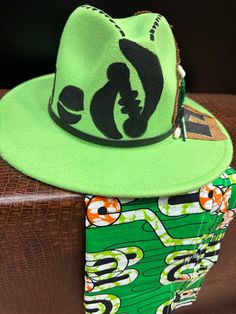 A Green fedora with scarf. The two are a hit. This l fedora is featured with feathers to make a statement. The fedora has ribbon inside to ensure proper fit. Don't delay order yours today. Green Fedora For Festivals, Green Fedora For Festival, Winter Fedora, African Kimono, Cowrie Shell, Fedora Hat, Leather Band, Fedora, Cowboy Hats