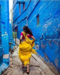 a woman in a yellow sari walking down an alleyway with blue painted walls